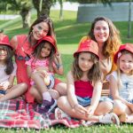 Friends enjoying a sunny day picnic on grass with bucket hats and smiles in a Portuguese park.